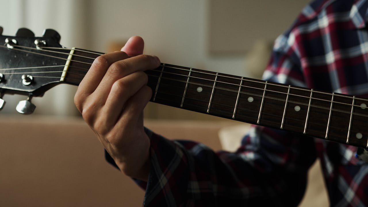 Person fingerpicking an acoustic guitar in a close-up shot.