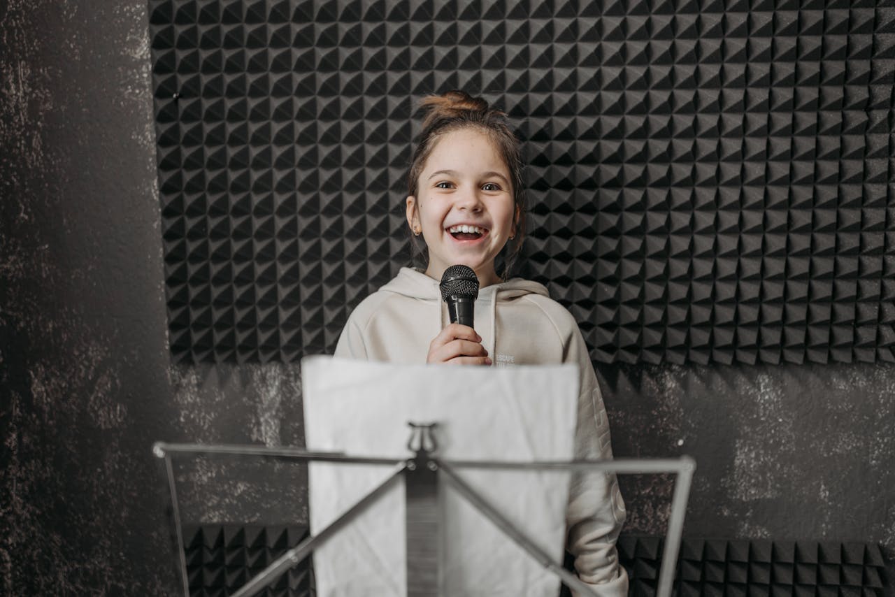 Young girl singing into a microphone during a music lesson in a studio.