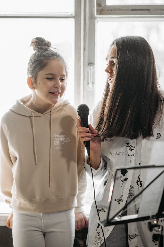 A student and teacher share a microphone during a singing lesson indoors.